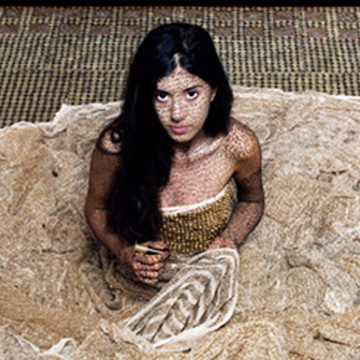 a woman sits on the floor with her gown around her in a circle. She is looking up toward the viewer with a serious expression on her face