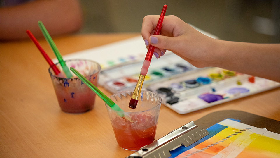 A child's hand dipping a paint brush in a cup of water